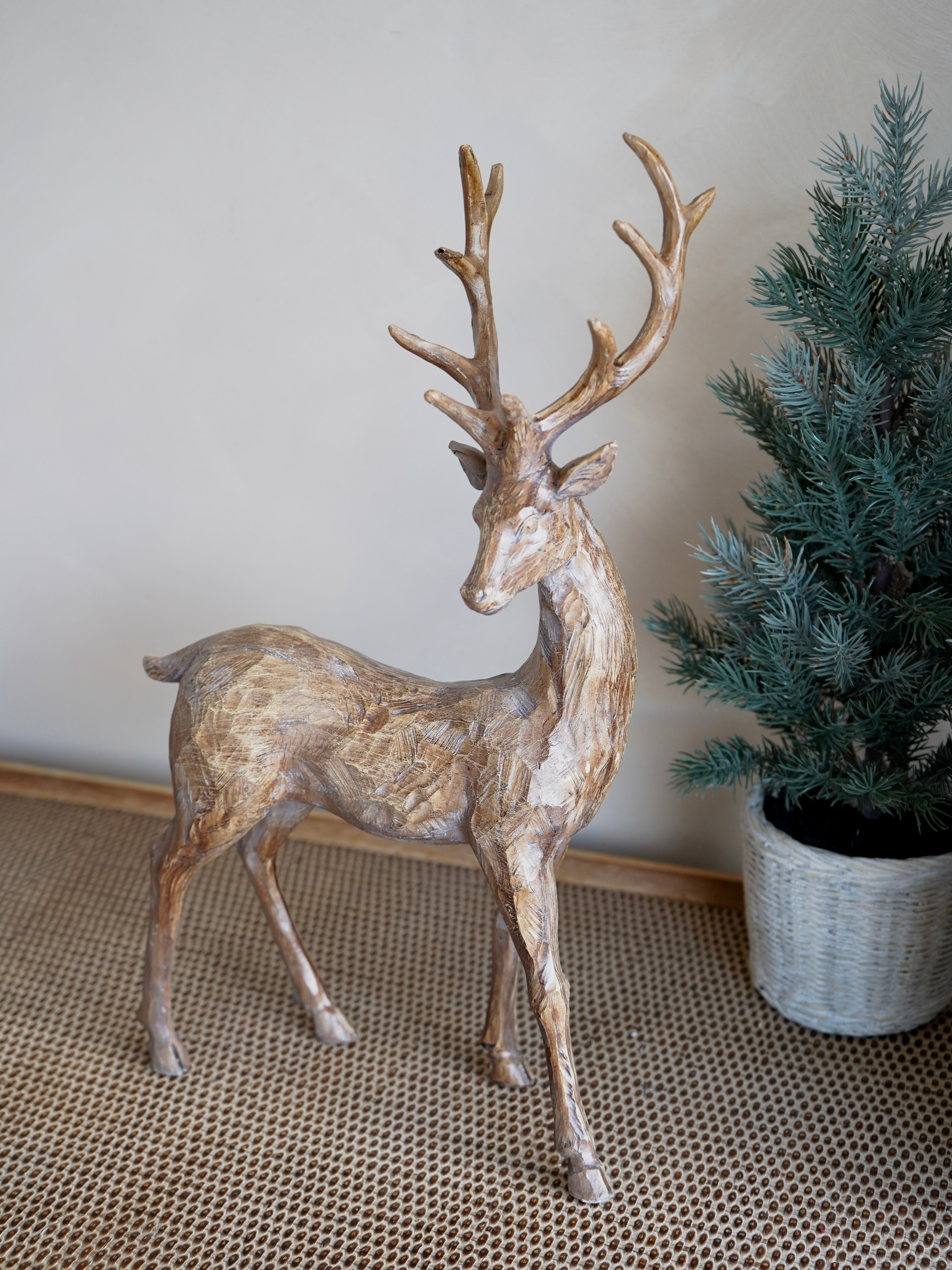 Decorative deer statue on a textured floor with a plant in the background