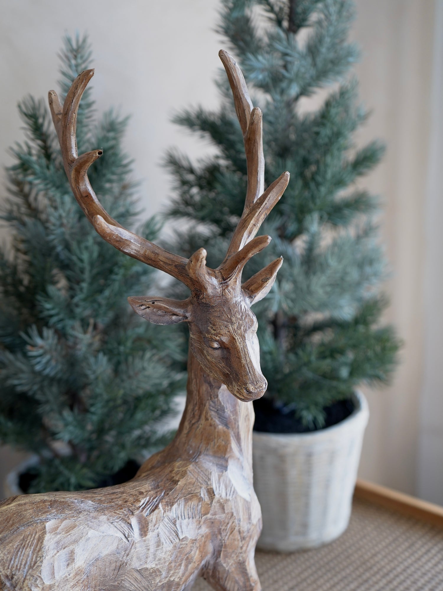 Wooden deer figurine with antlers in front of a potted Christmas tree.