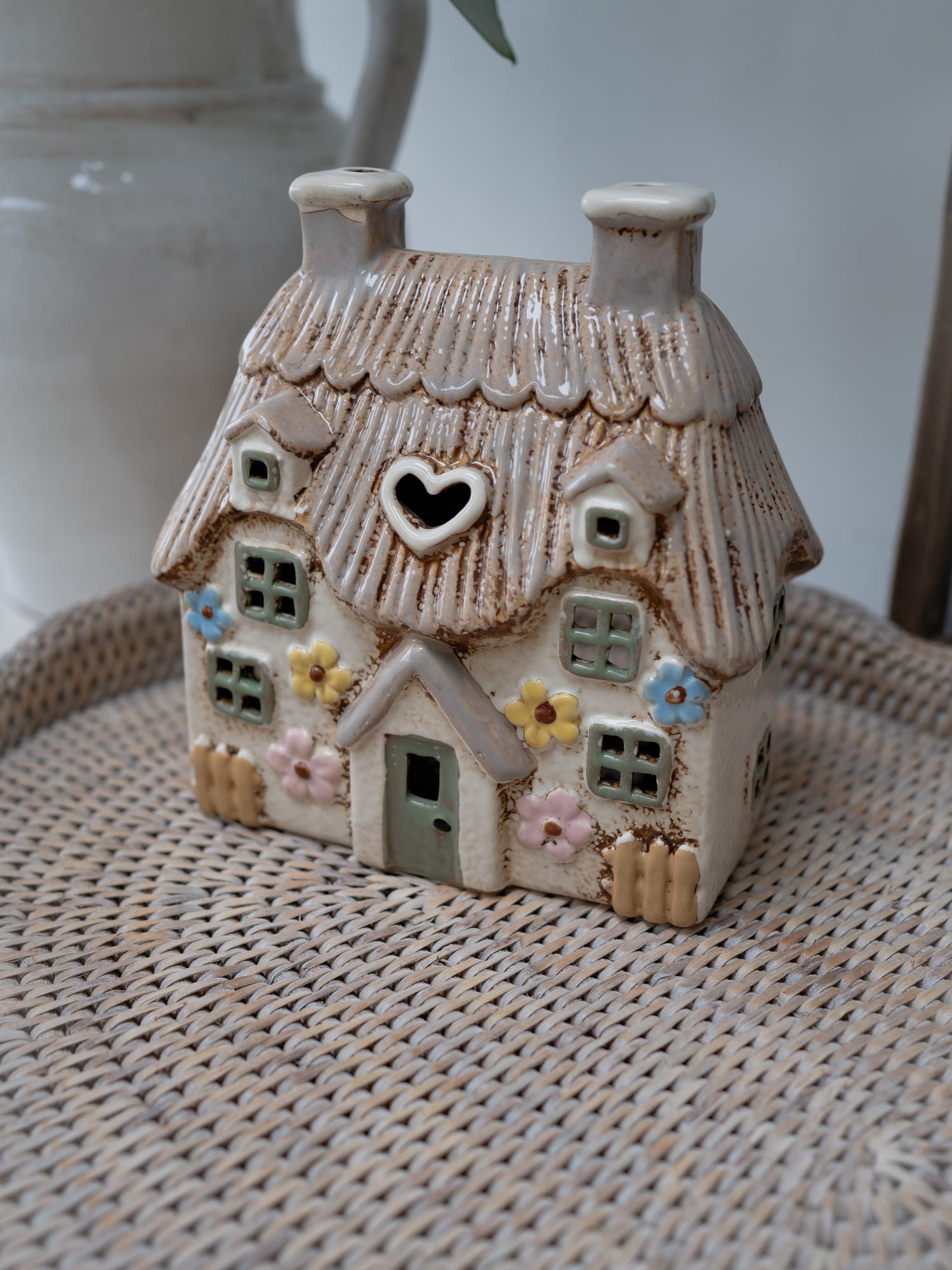 Small ceramic house with a heart window on a woven surface