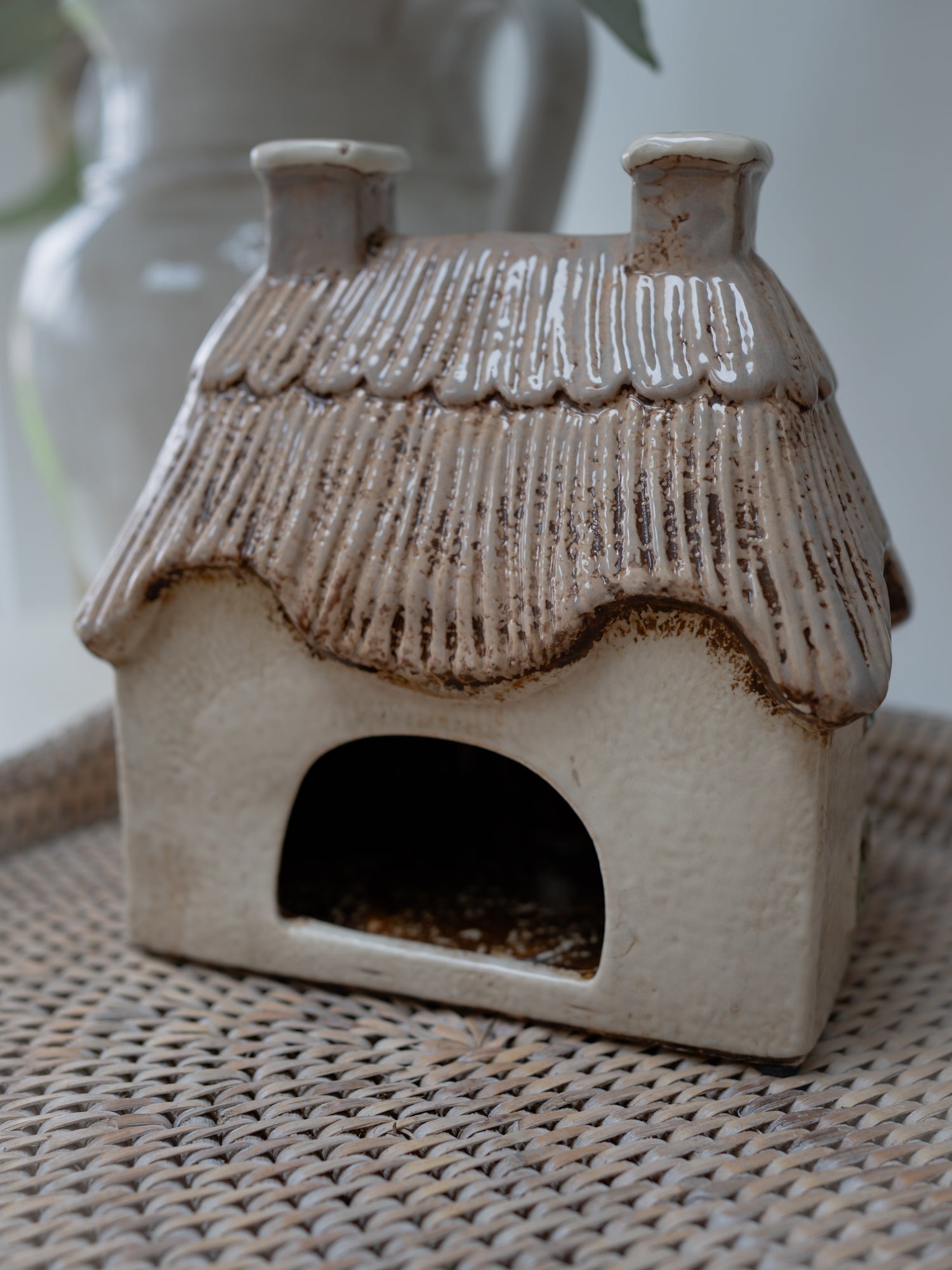 Ceramic birdhouse with a textured roof on a woven surface