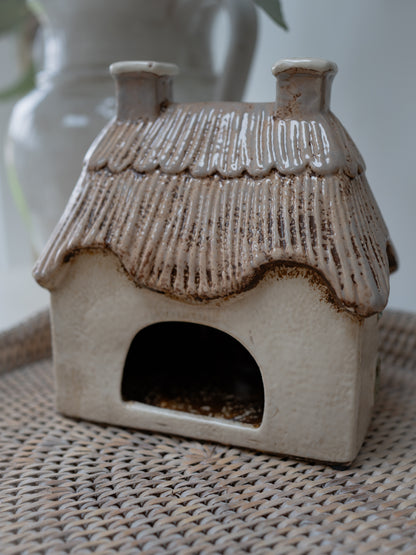 Ceramic birdhouse with a textured roof on a woven surface