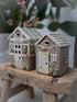 Two small ceramic houses on a wooden surface with a blurred floral background