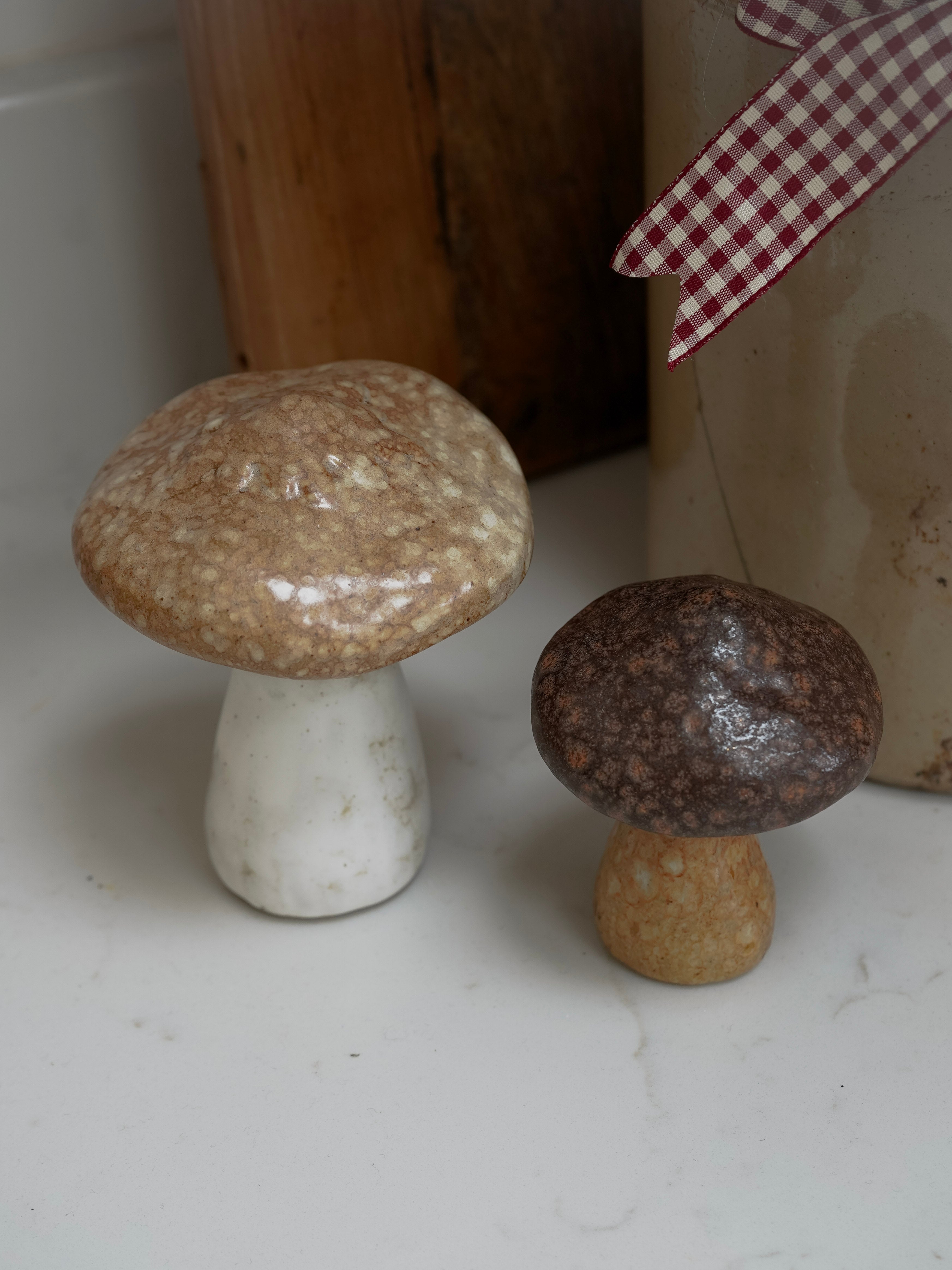 Two decorative mushrooms on a white surface with a checkered cloth in the background.