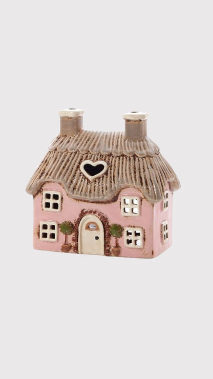 Small pink cottage tea light holder with a thatched roof on a white background