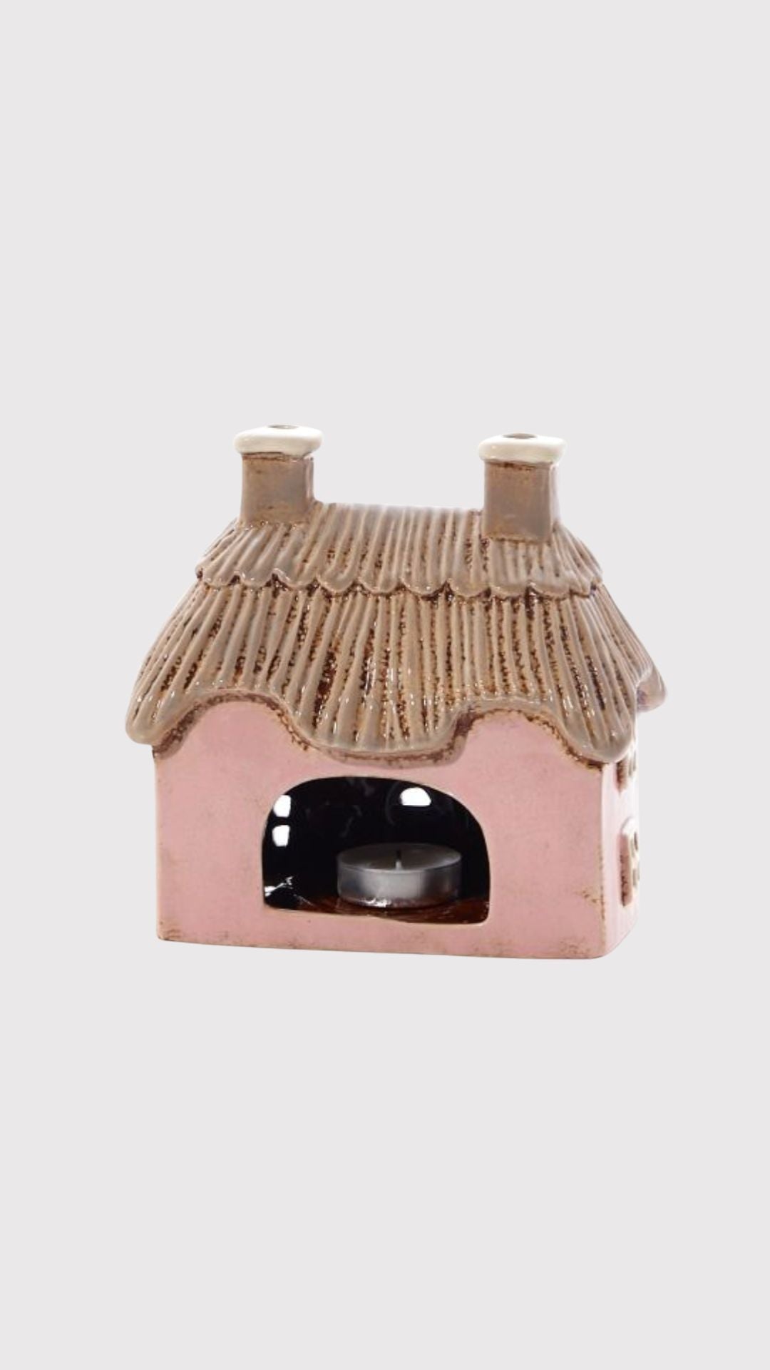 Pink cottage-shaped candle holder with a thatched roof on a white background