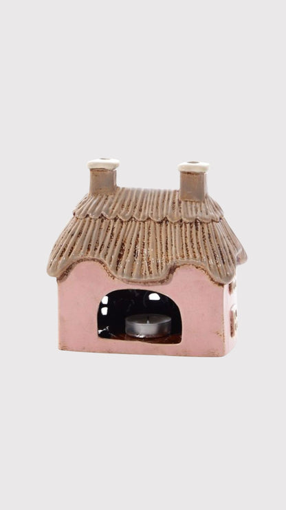 Pink cottage-shaped candle holder with a thatched roof on a white background