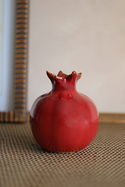 Red ceramic pomegranate-shaped vase on a textured surface with a neutral background