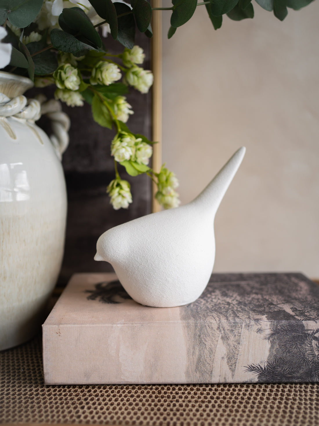 White stoneware bird figurine on a textured surface with greenery in the background