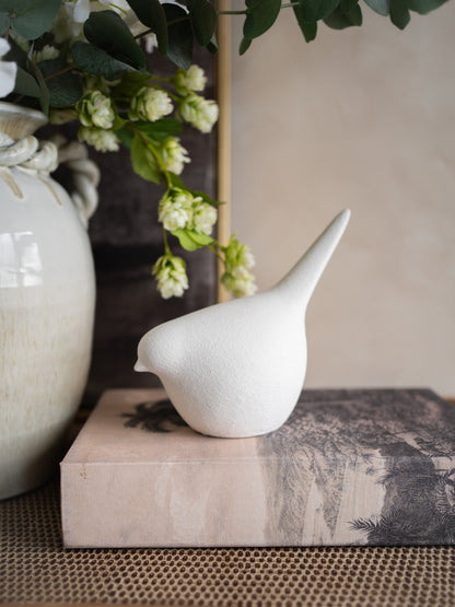 White stoneware bird figurine on a textured surface with greenery in the background