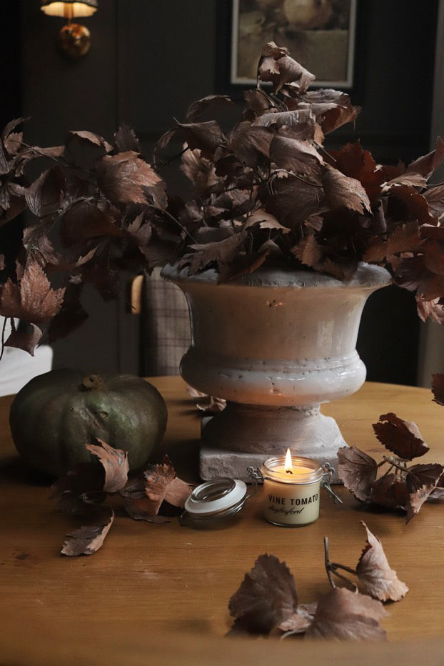 Decorative setup with dried leaves, a candle, and a pumpkin on a wooden surface.