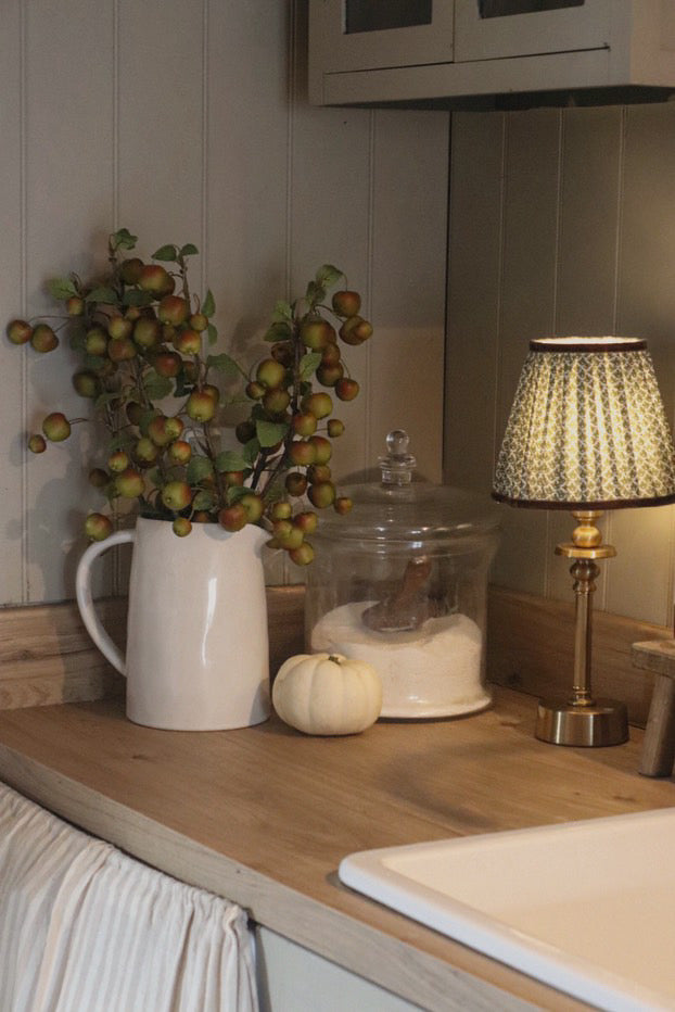 Kitchen counter with a white pitcher, small pumpkin, and decorative lamp.