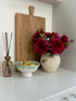 Decorative items including a vase with red flowers, a wooden cutting board, and a diffuser on a white surface.