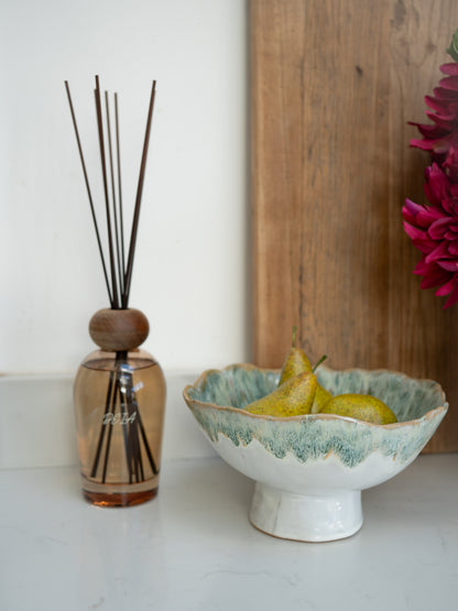 Decorative bowl with pears next to a luxury reed diffuser on a white surface