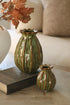 Two green ceramic green  poppy head vases on a surface with a book and decorative leaves.