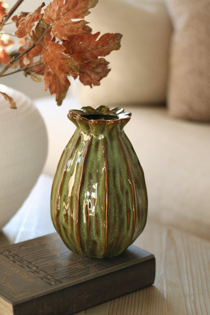 Green ceramic poppy head vase on a wooden surface with a blurred background