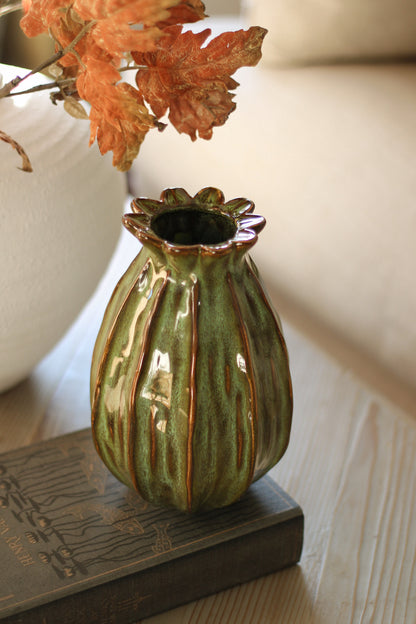 Green ceramic poppy head vase with ribbed texture on a wooden surface
