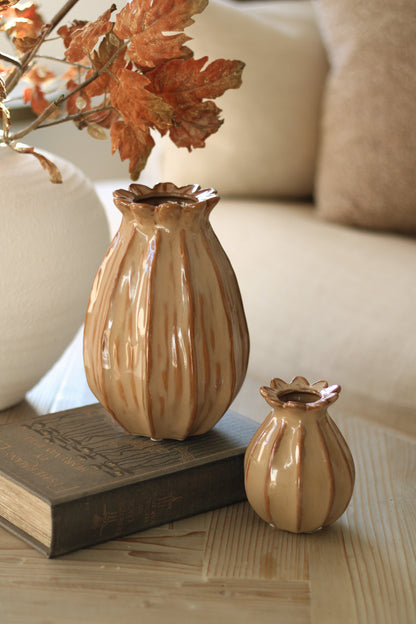 Two ceramic poppy head vases on a wooden surface with a blurred background