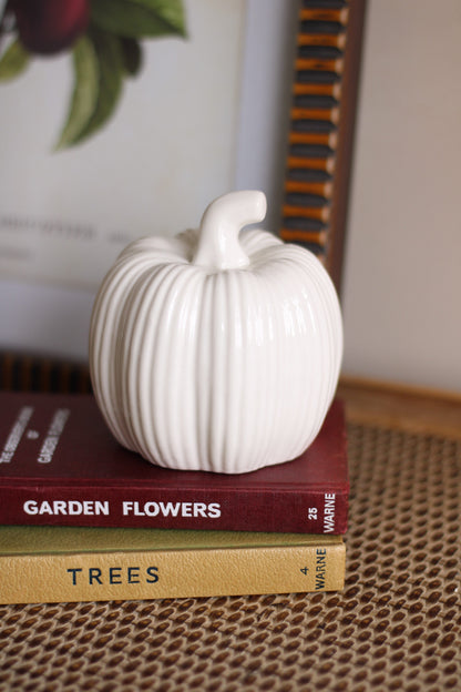 White ceramic pumpkin on top of two books with visible titles.