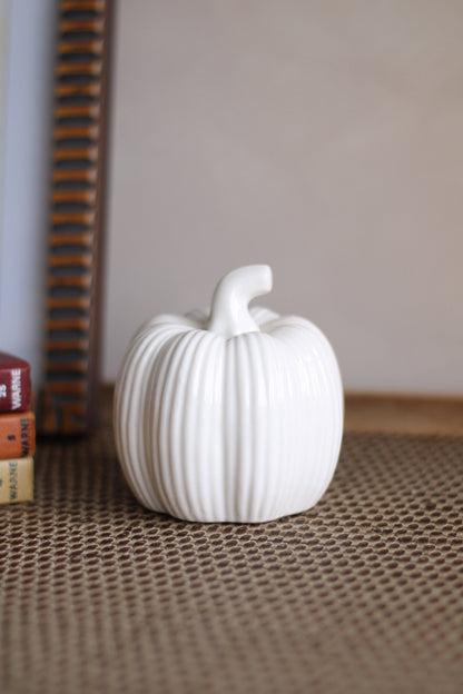 White ceramic pumpkin on a textured surface with a neutral background