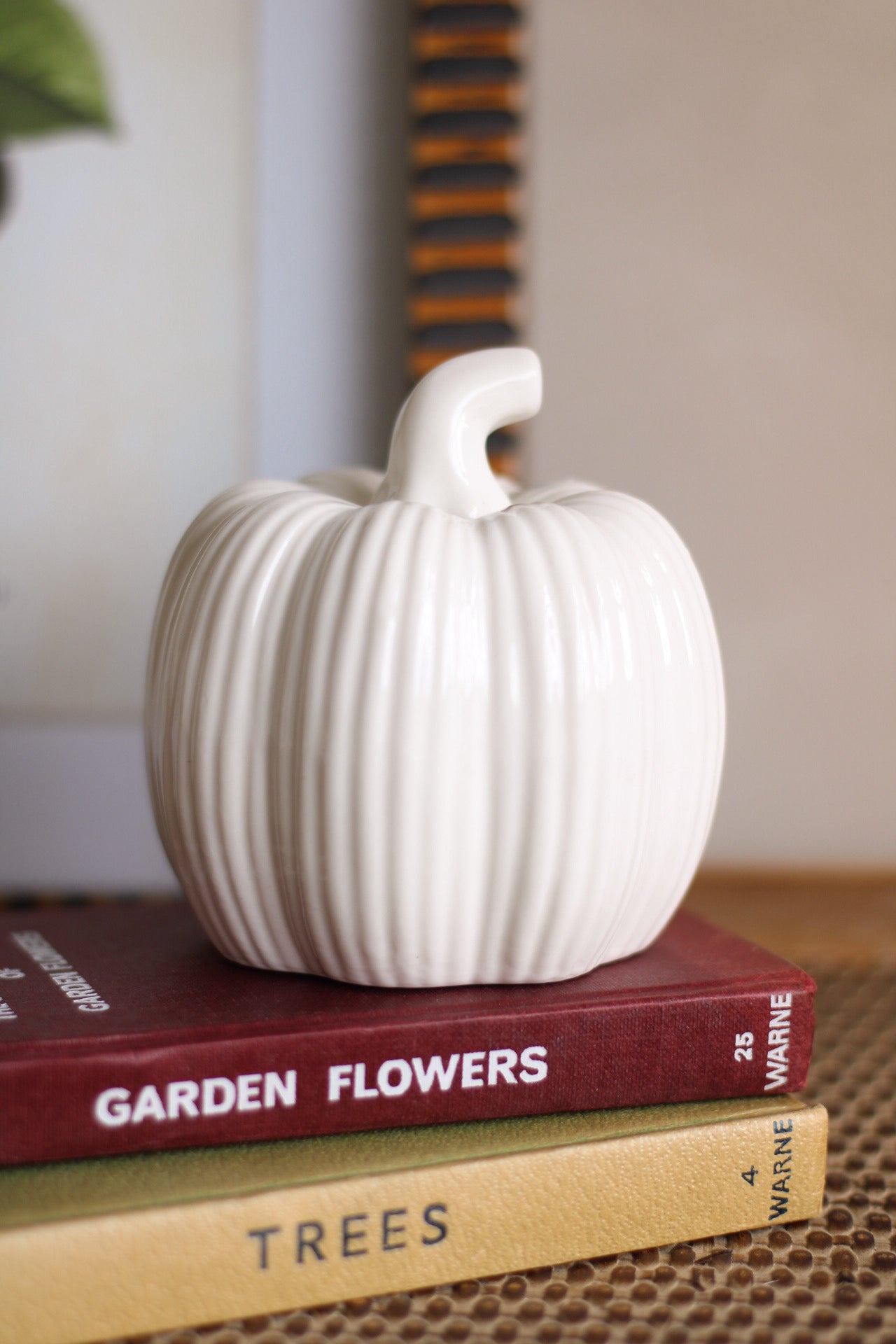 White ceramic pumpkin on top of two books with visible titles.