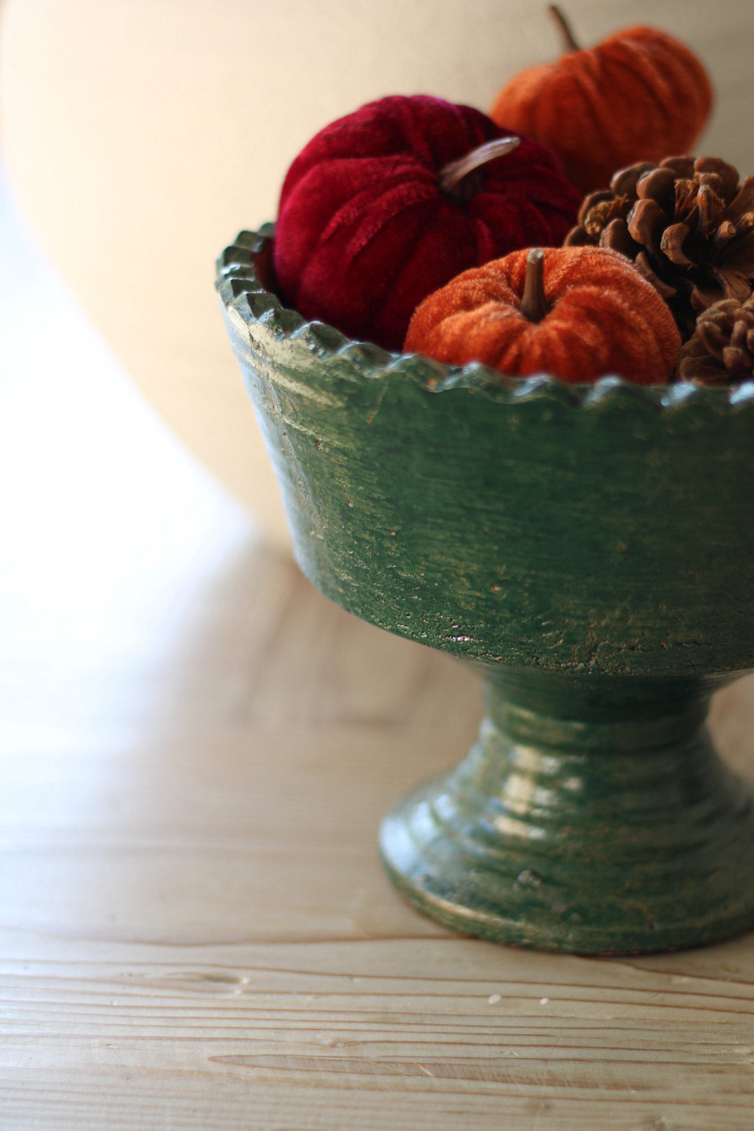 Green decorative bowl with small pumpkins and pinecones on a light wooden surface