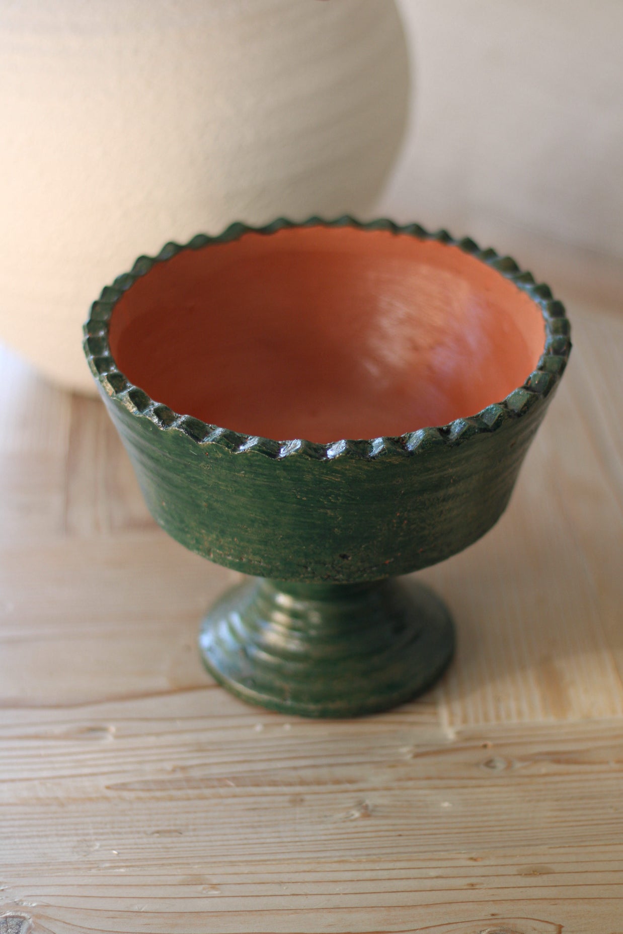Terracotta bowl with green exterior and red interior on a wooden surface