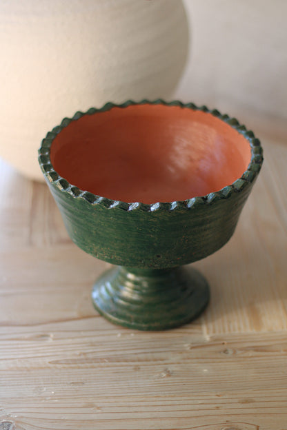 Terracotta bowl with green exterior and red interior on a wooden surface