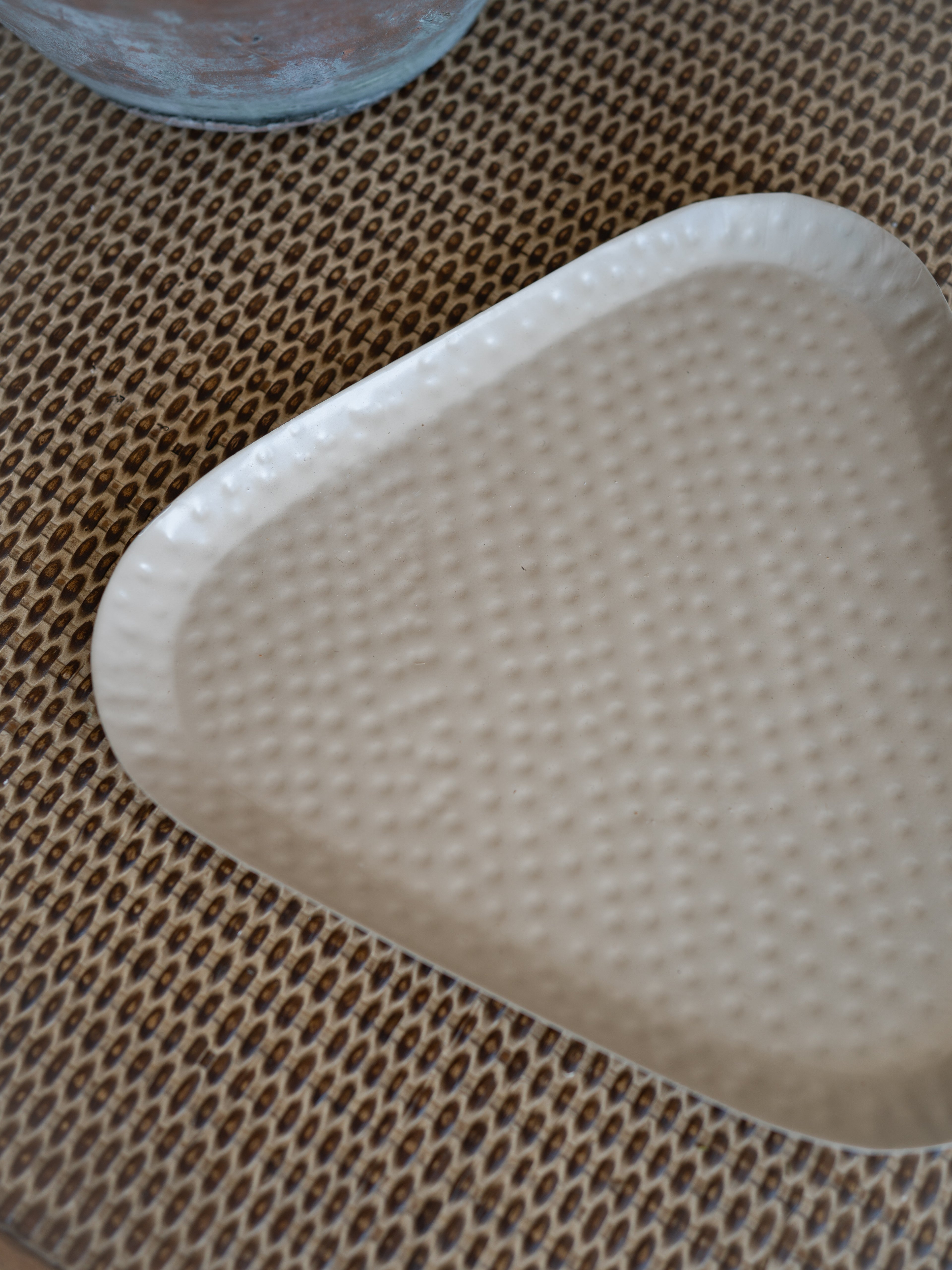 A triangular metal tray with a textured, dimpled surface, shown on a brown woven placemat.