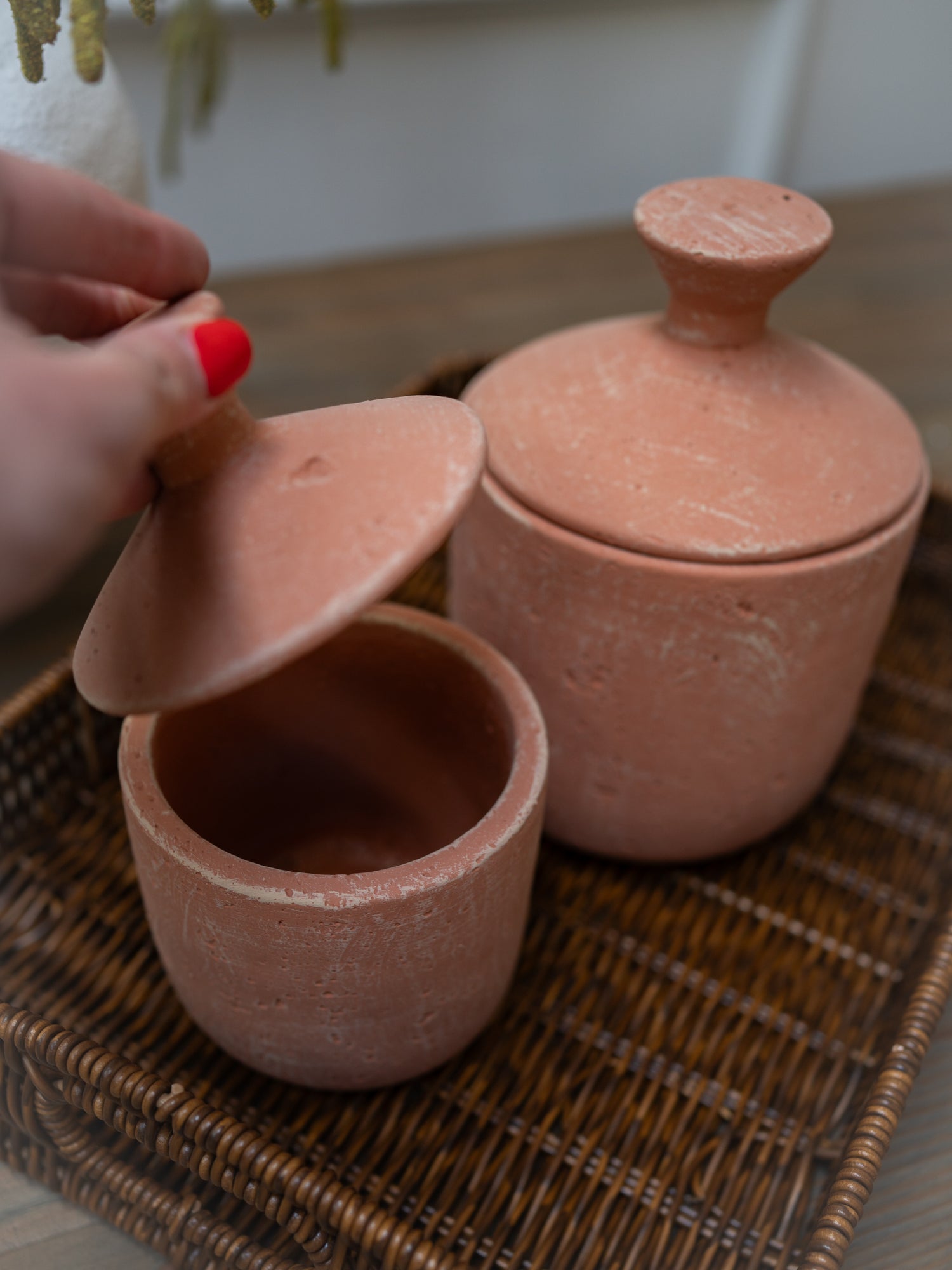 Two terracotta pots with lids on a woven surface.