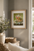 Framed artwork of a floral basket on a wall in a room with decor elements.