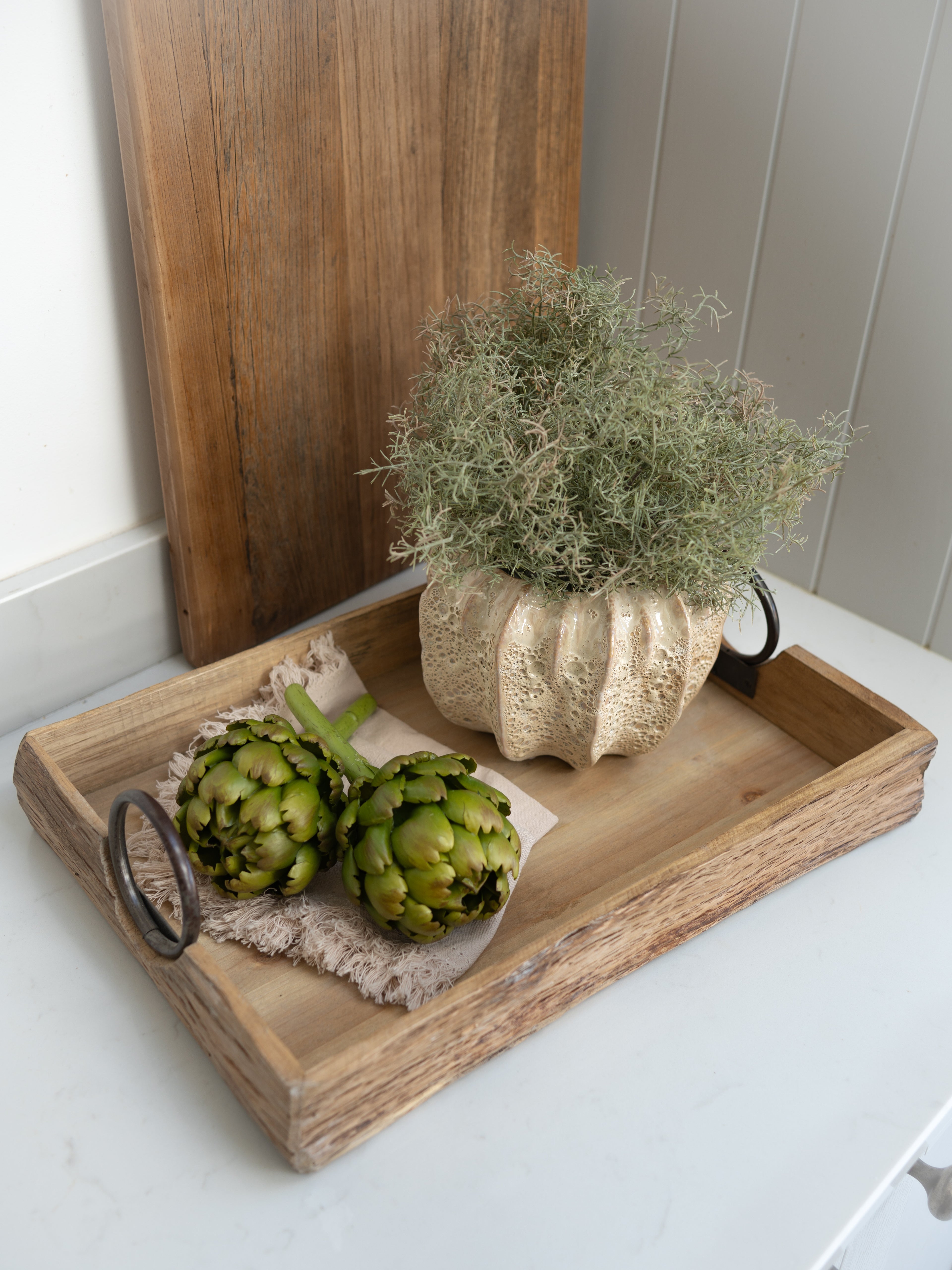 Wooden tray with artichokes and a small plant pot with spanish moss on a white surface.