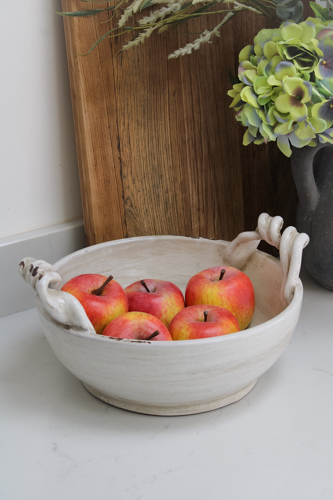 Twisted handle cream ceramic decorative fruit bowl filled with faux red apples