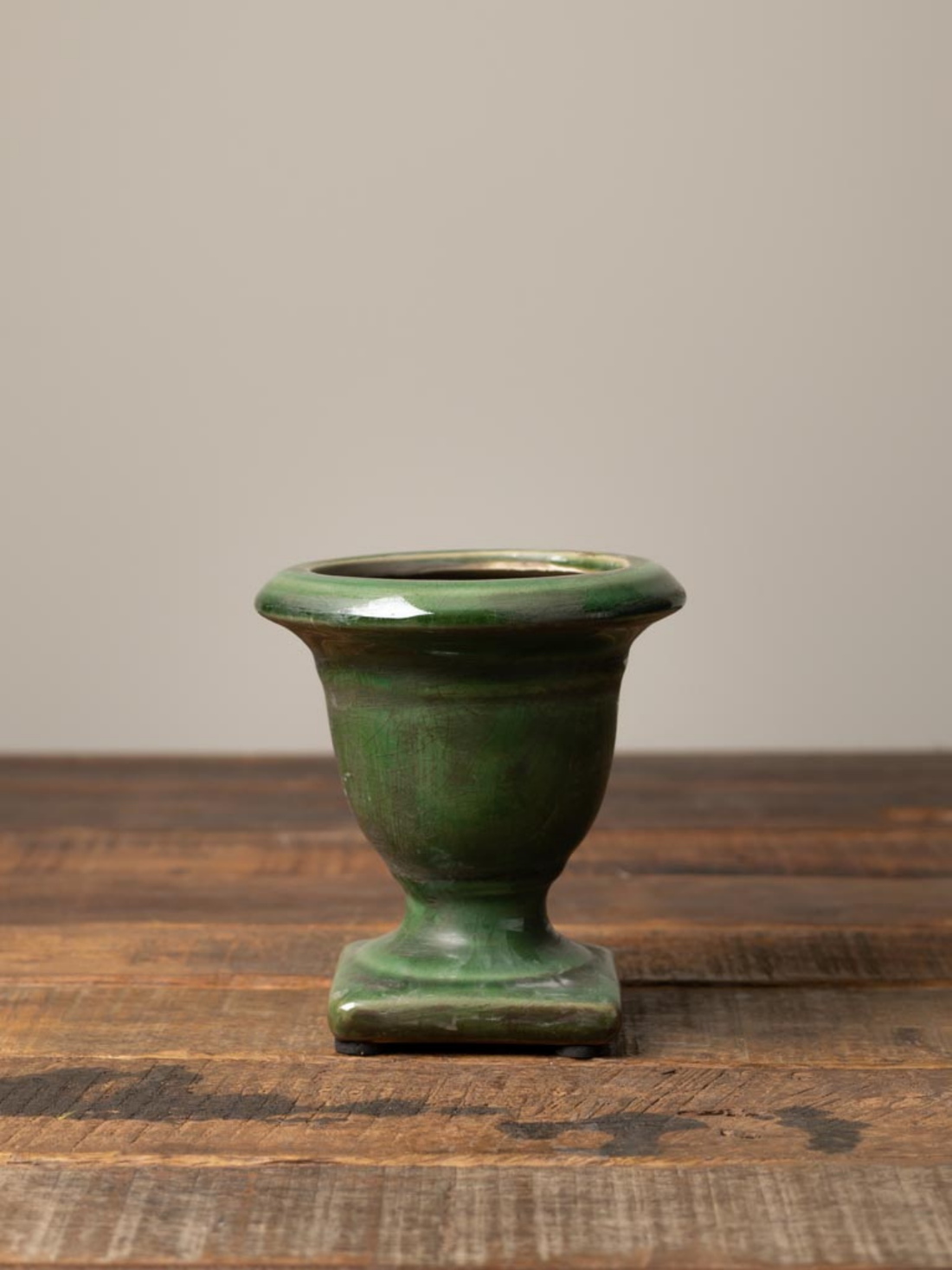 Green ceramic vase on a wooden surface with a neutral background