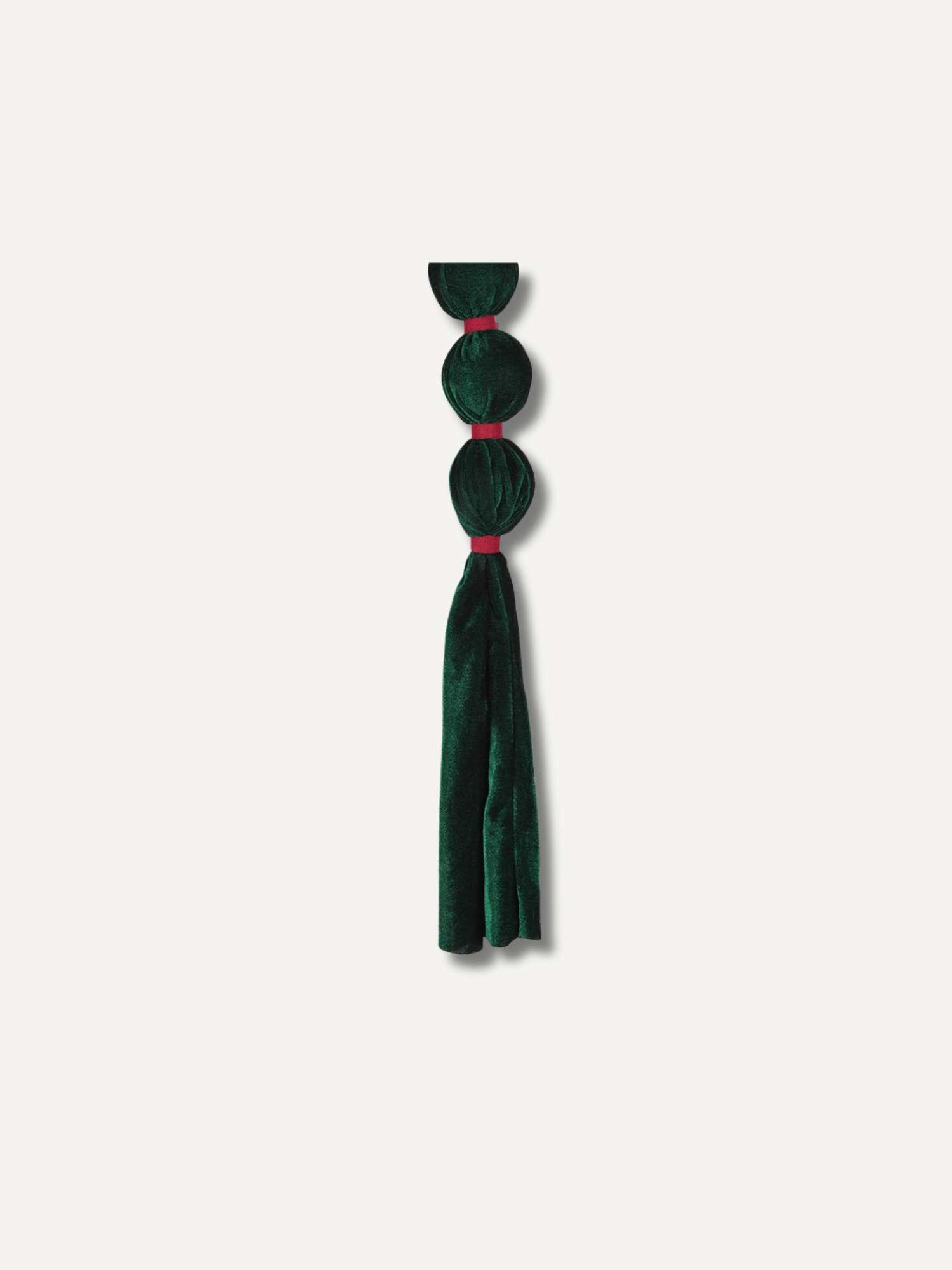 A dark forest green velvet tassel accessory with three circular bead-like loops connected by thin red bands, shown against a solid off-white background.