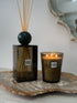A Sences Verde diffuser set featuring a dark green glass reed diffuser bottle with a green marble sphere and reeds, alongside a matching lit candle in a glass holder, both resting on a rustic wood slice tray.