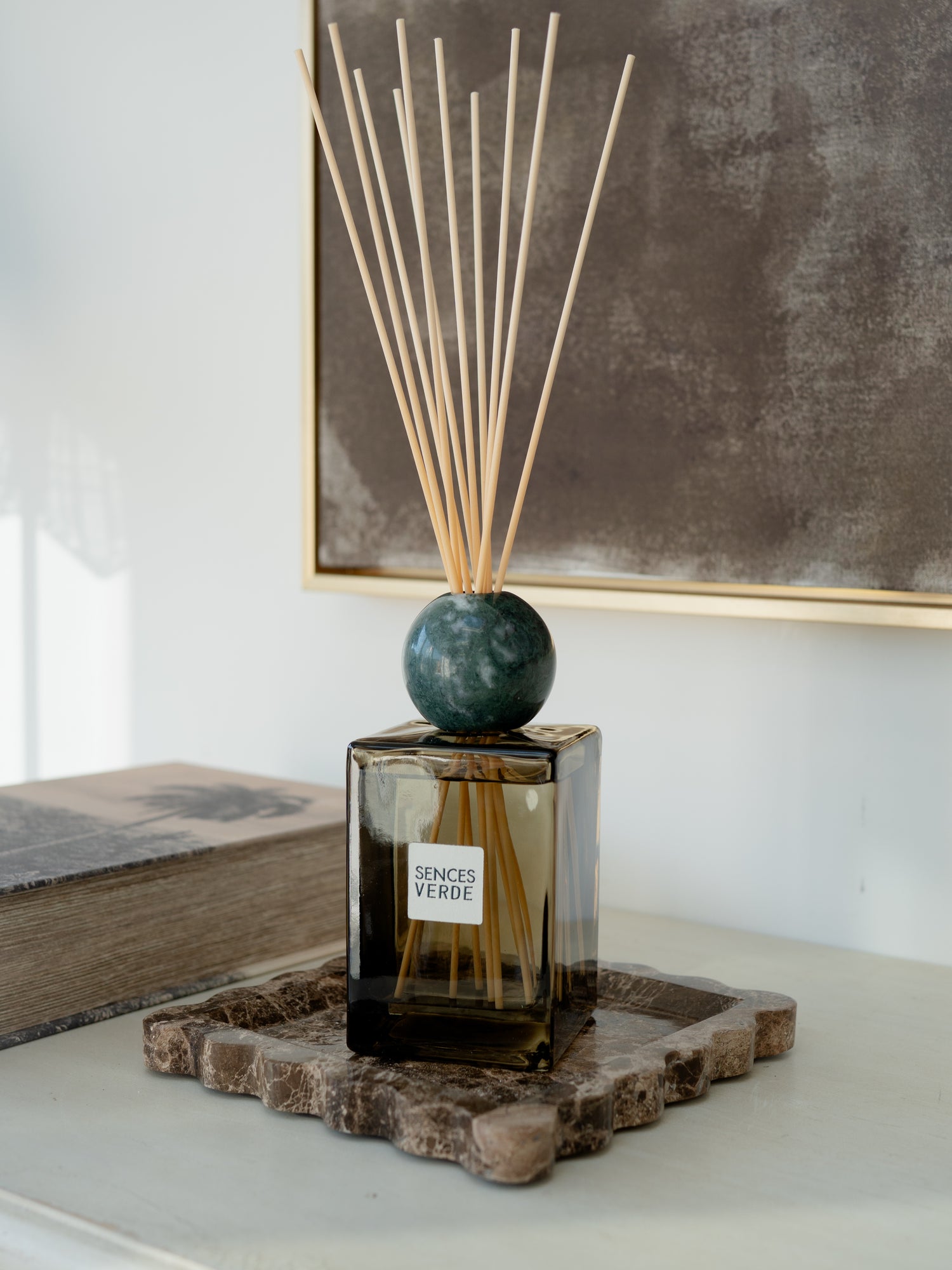 A reed diffuser bottle with a dark green marble sphere and natural reeds, placed on a stone tray in a styled interior setting.
