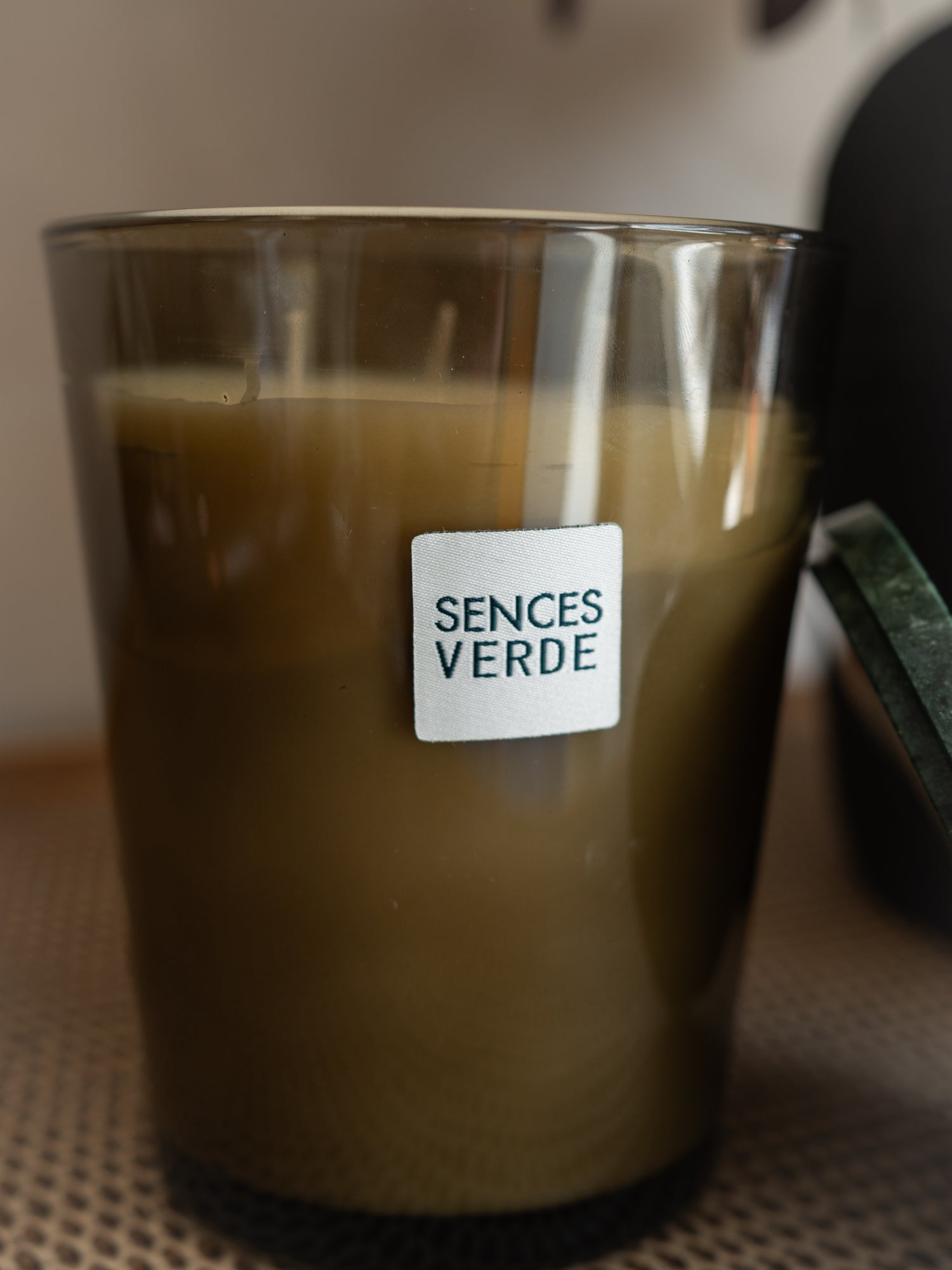 A close-up of a candle in a smoky amber glass jar with a white label reading &