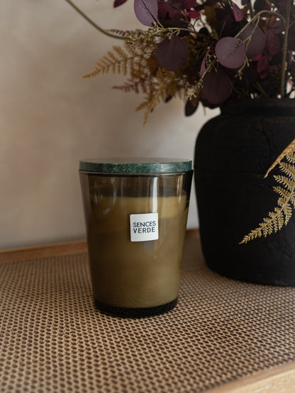 A candle in a dark amber glass jar with a green marble-patterned lid, labeled &