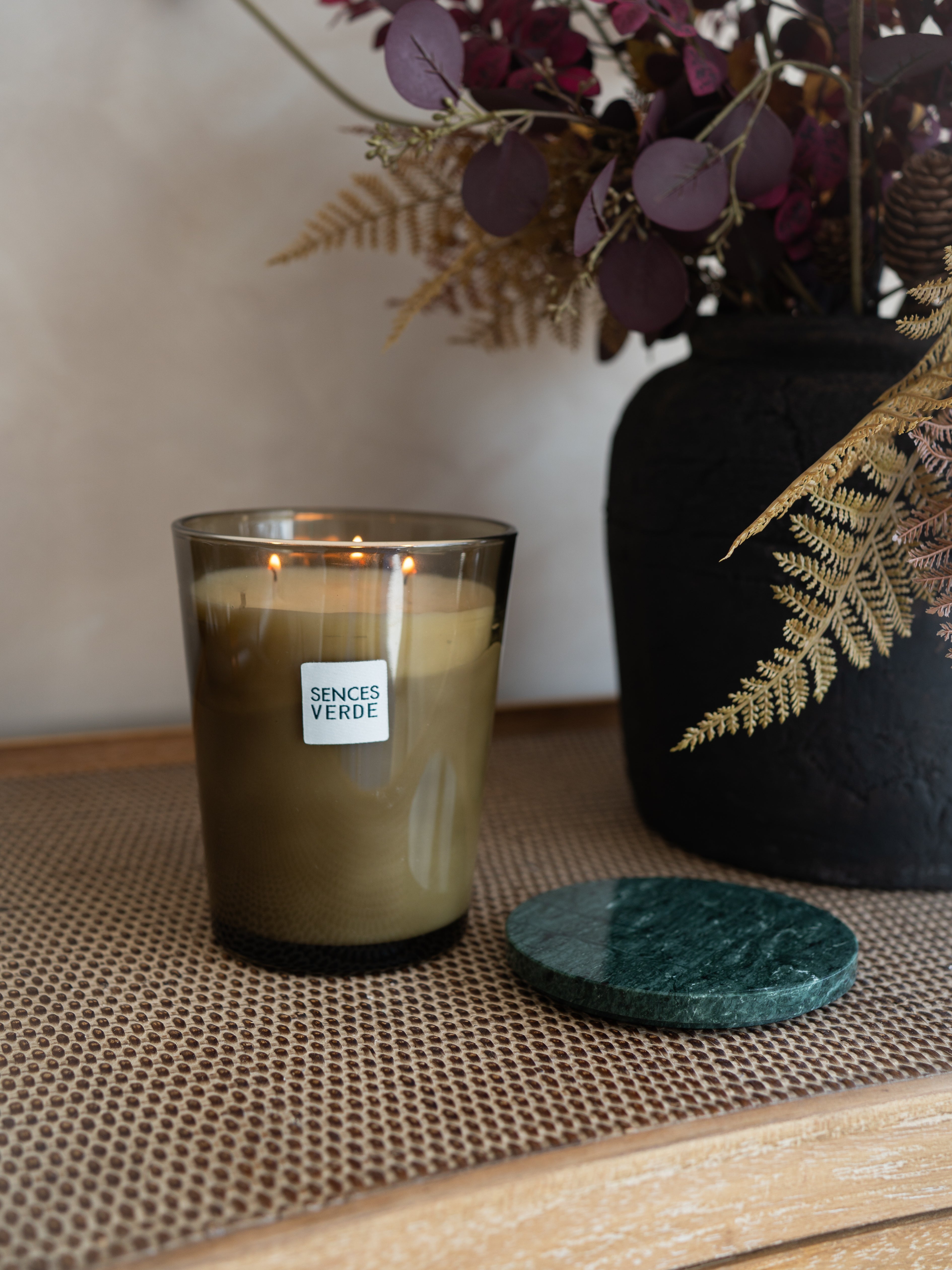 A lit candle in a smoky amber glass jar with a white label reading &
