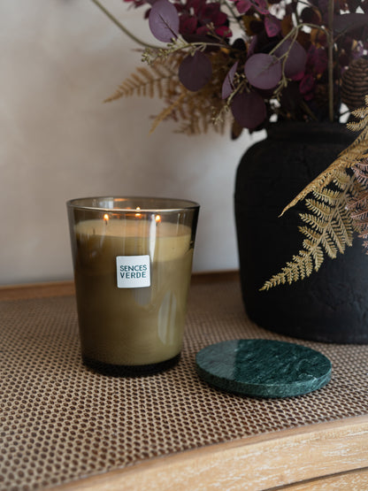 A lit candle in a smoky amber glass jar with a white label reading &