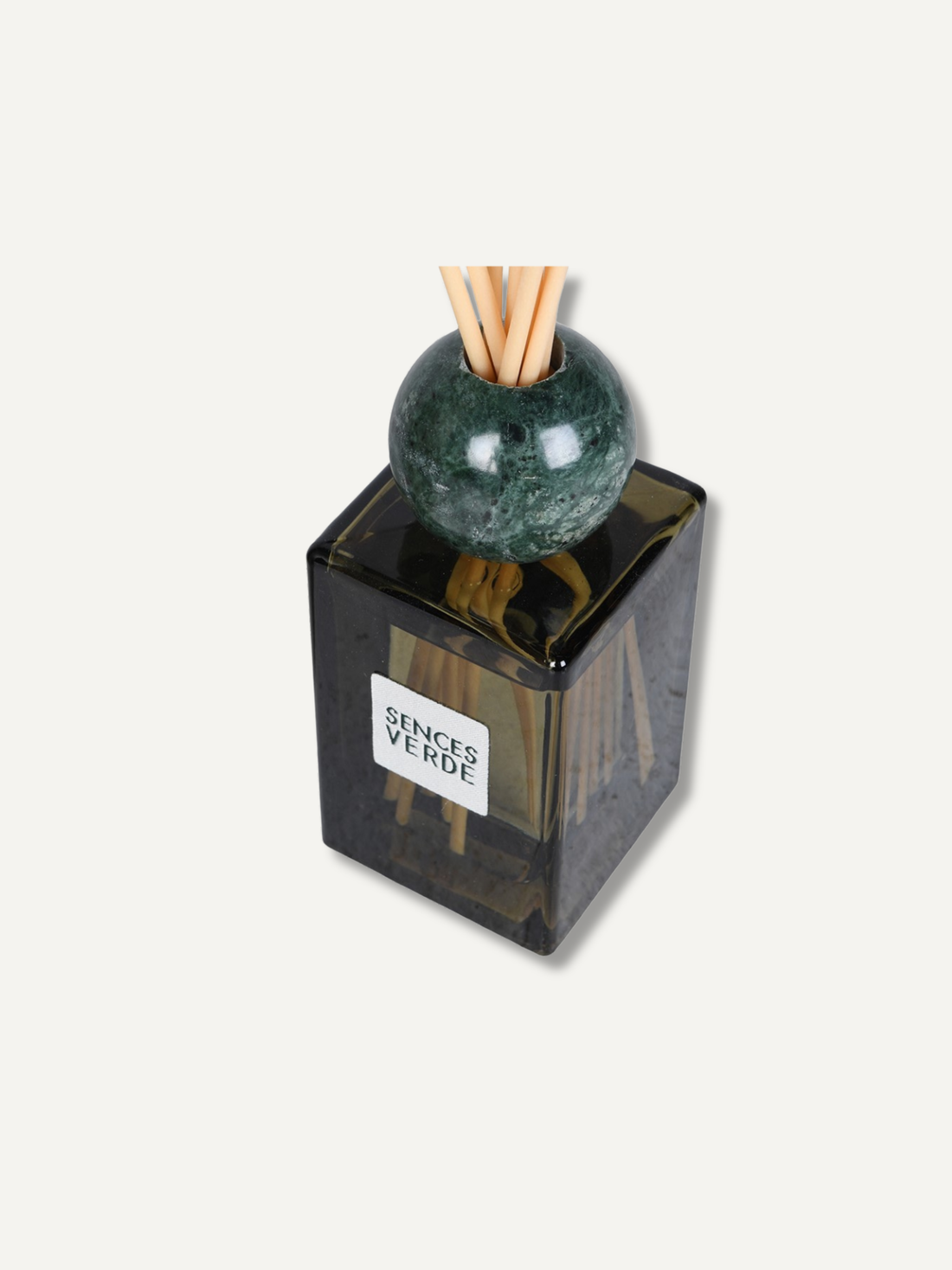 A reed diffuser bottle with a dark translucent square glass body, a green marble sphere, and natural reed sticks, with a white label reading &