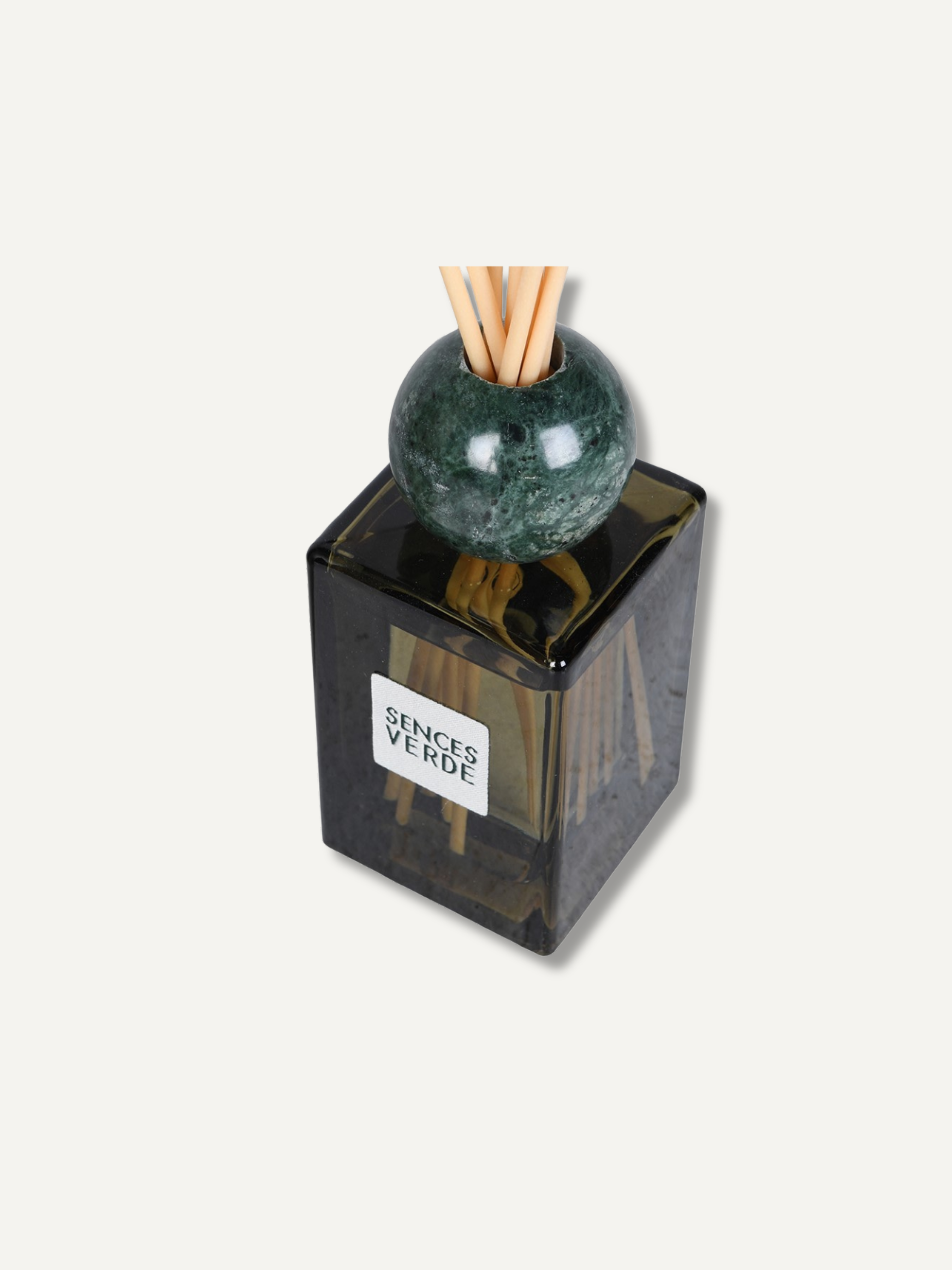 A reed diffuser bottle with a dark translucent square glass body, a green marble sphere, and natural reed sticks, with a white label reading &