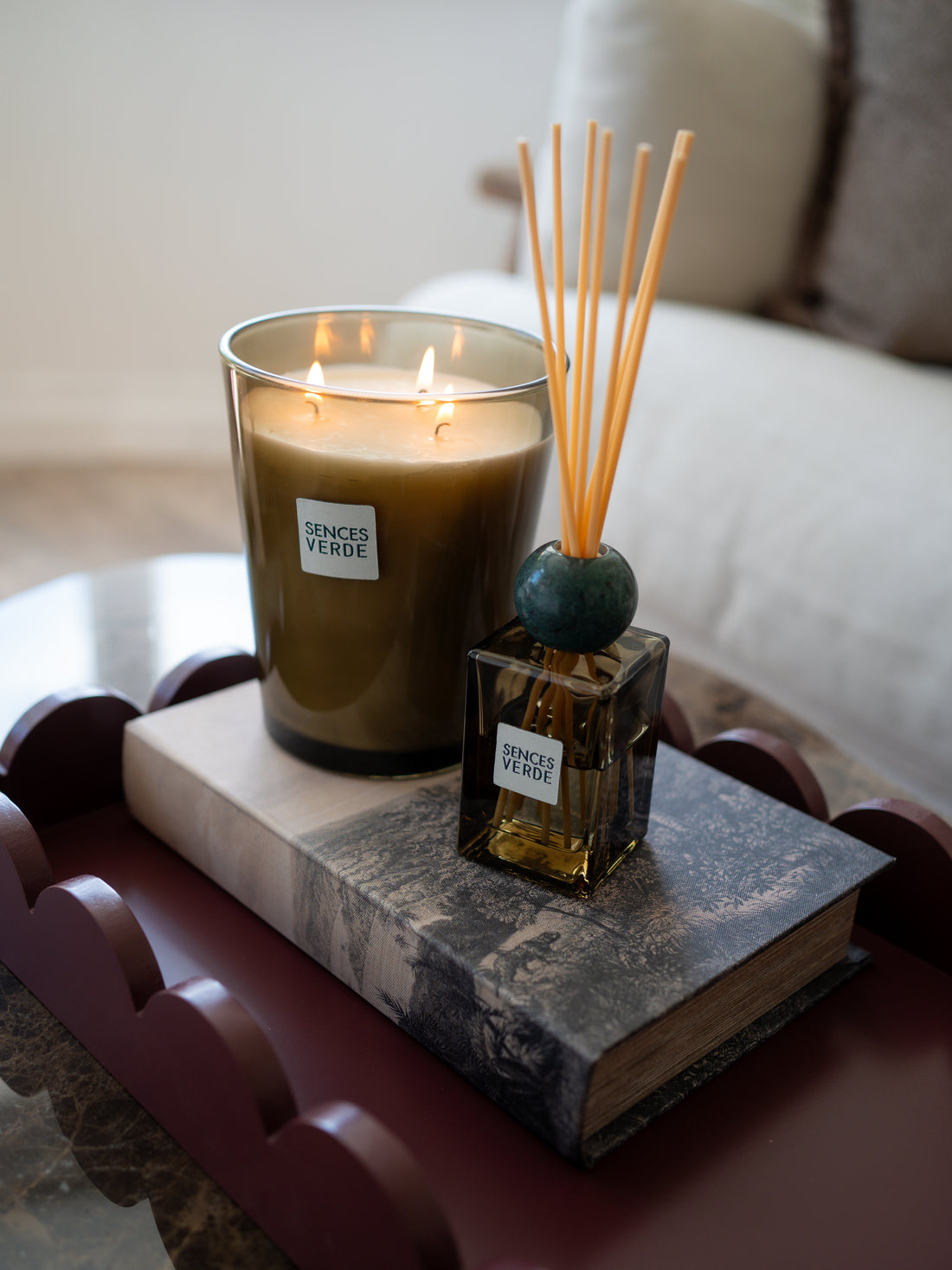 A lit candle in a clear glass jar and a reed diffuser bottle with wooden reeds, both labeled &