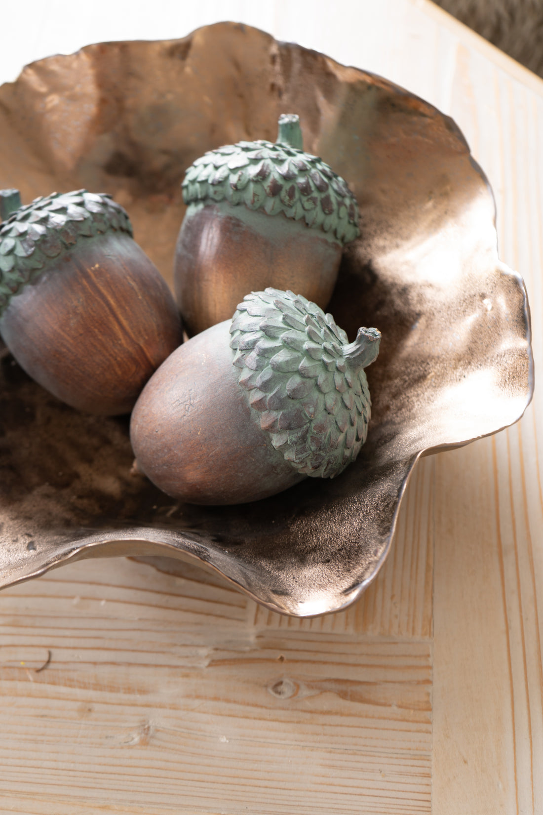 Three acorns in a decorative metal bowl on a wooden surface