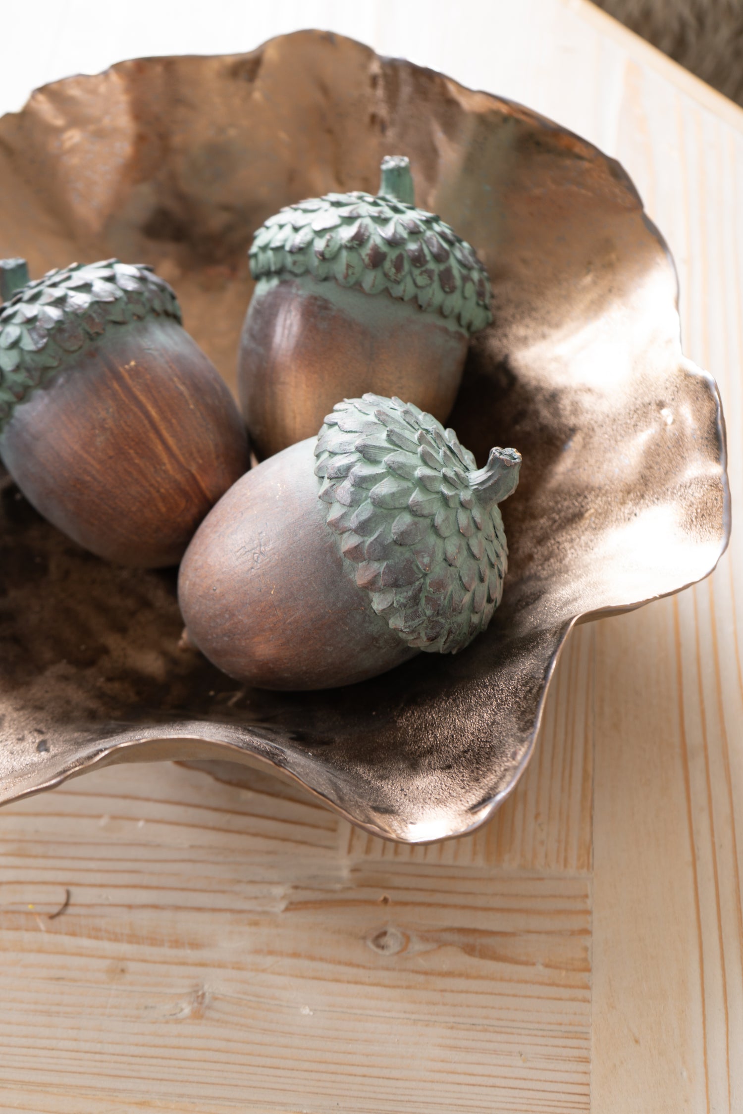 Three acorns in a decorative metal bowl on a wooden surface
