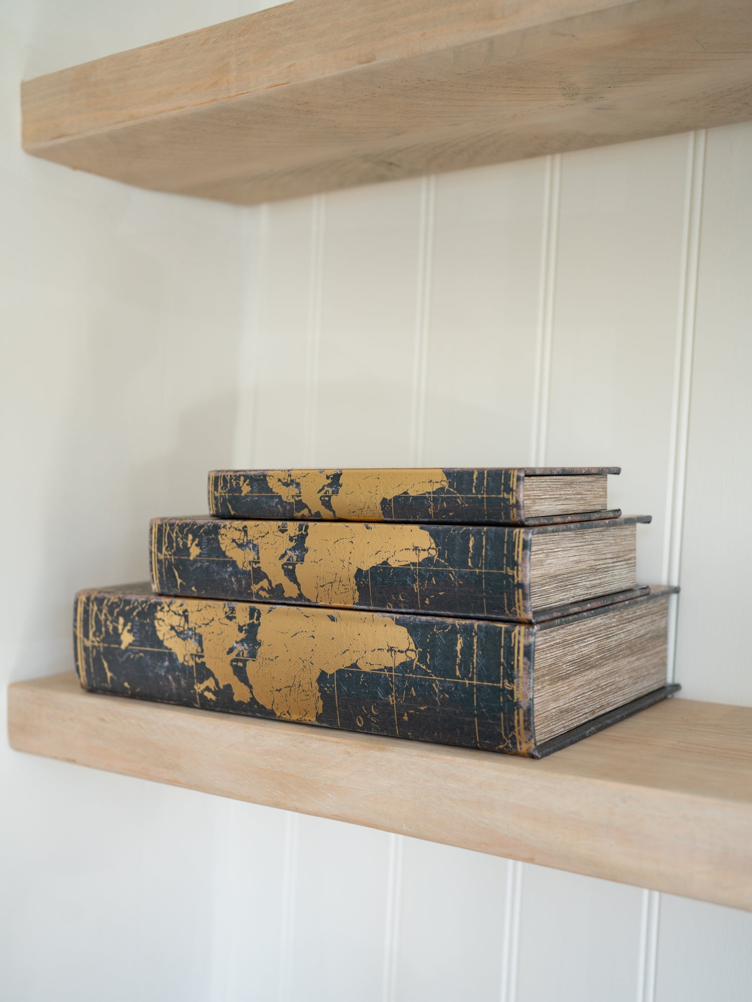 Stack of vintage storage books on a wooden shelf against a white paneled wall.
