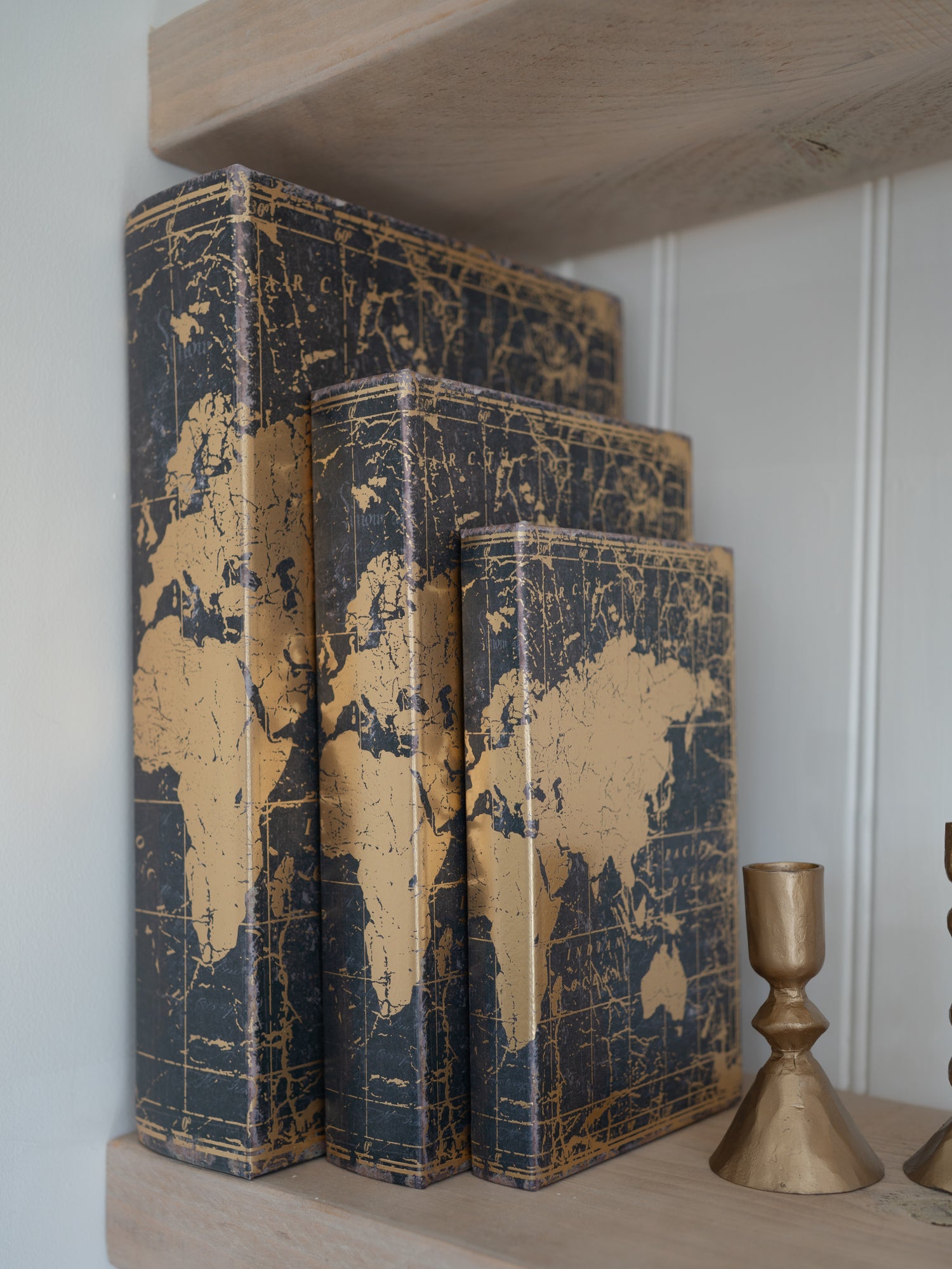 Three world map storage books stacked on a shelf with a gold candle holder.