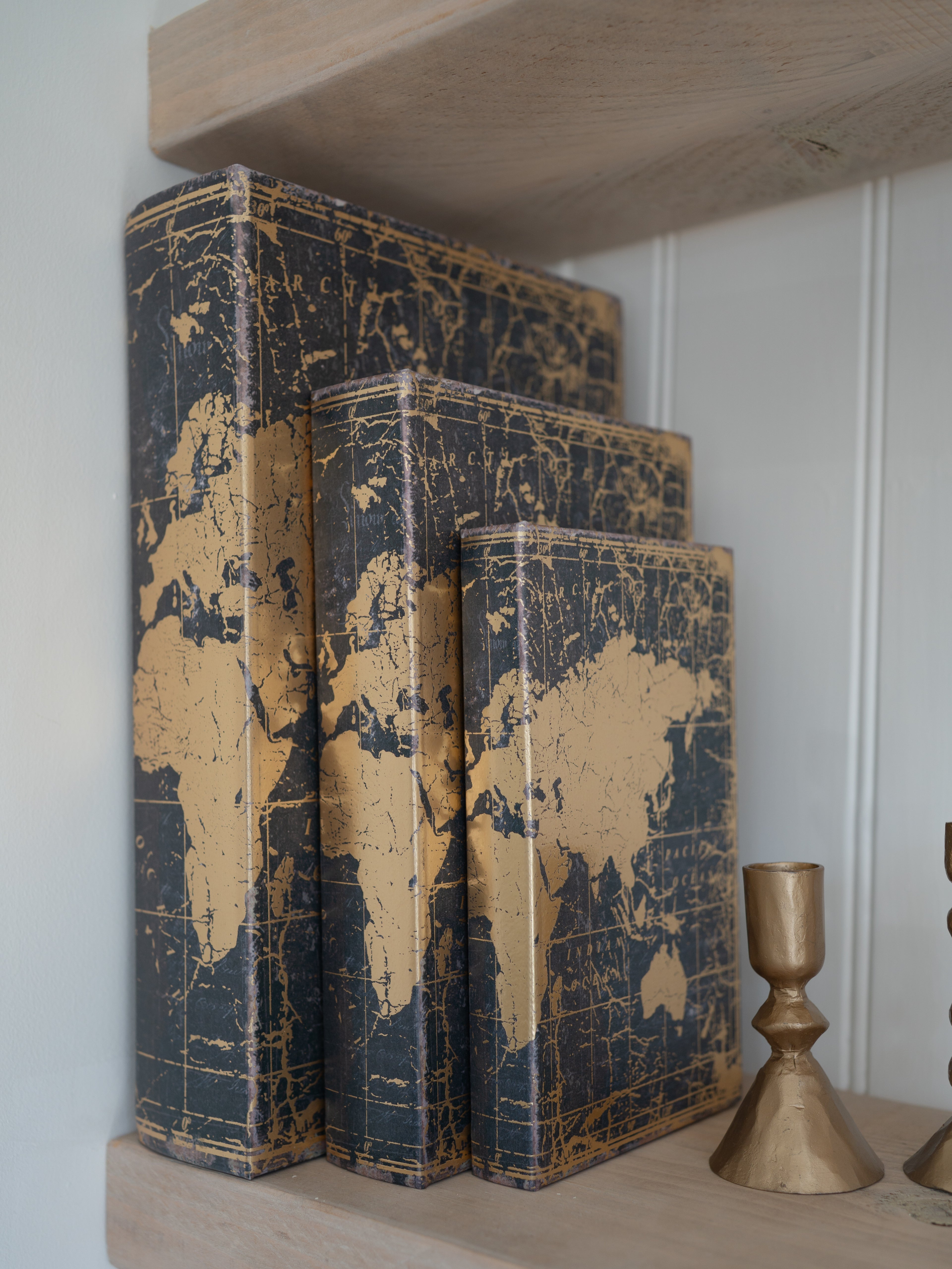 Three world map storage books stacked on a shelf with a gold candle holder.
