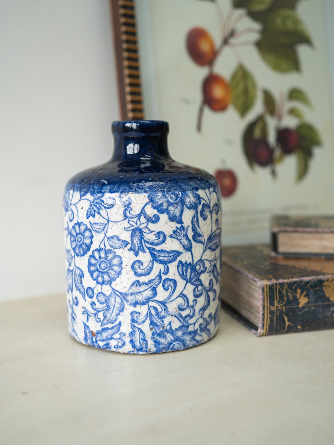 Blue and white patterned ceramic vase on a surface with books and a botanical illustration in the background.