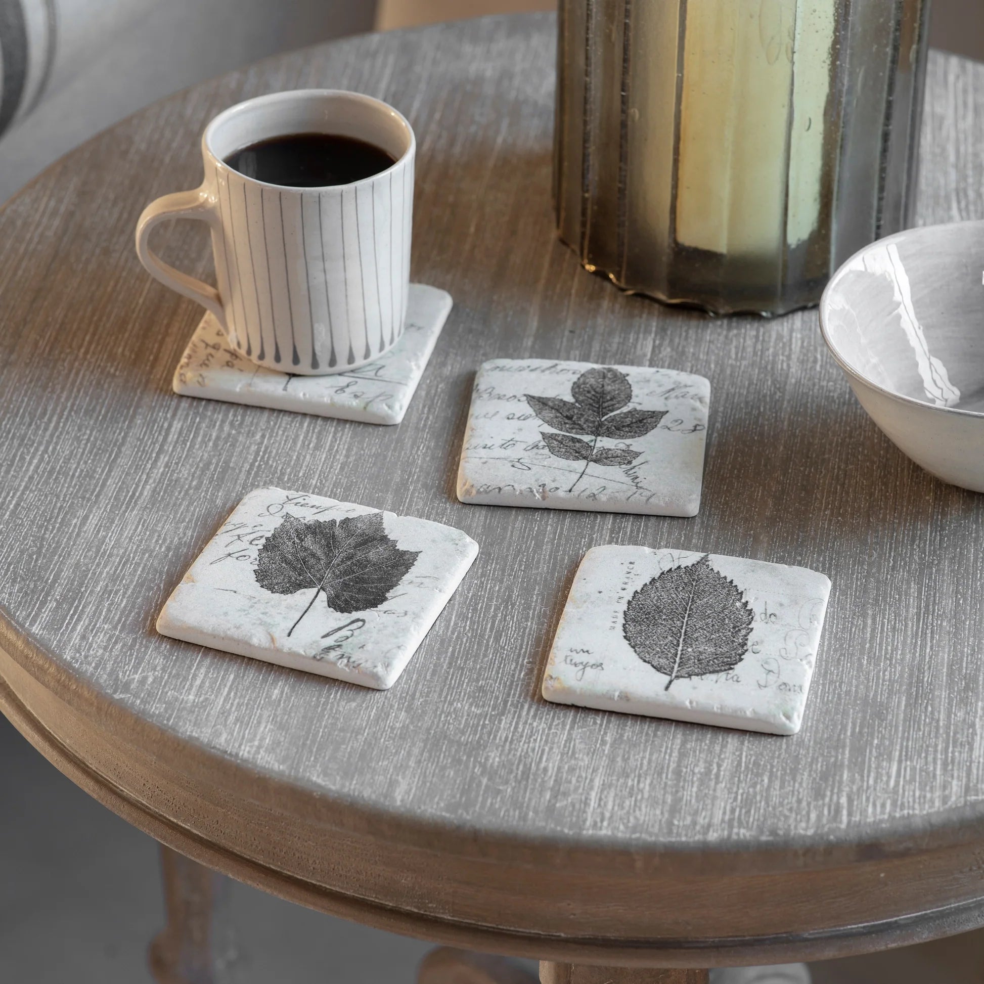 Coasters with leaf design on a round wooden table with a cup of coffee.